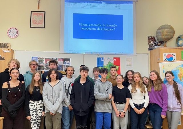Grupa uczniów stoi na tle tablicy z materiałami na temat Francji i języka francuskiego